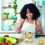 Healthy lifestyle. Good life. Organic food. Vegetables. Close up portrait of happy cute beautiful young woman while she try tasty vegan salad in the kitchen at home.