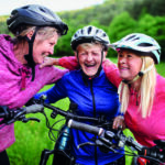 Happy active senior women friends cycling together outdoors in nature.