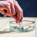 Hand stubbed out cigarette in a transparent ashtray