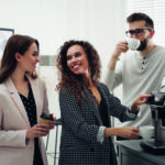 African American woman talking with colleagues while using modern coffee machine in office